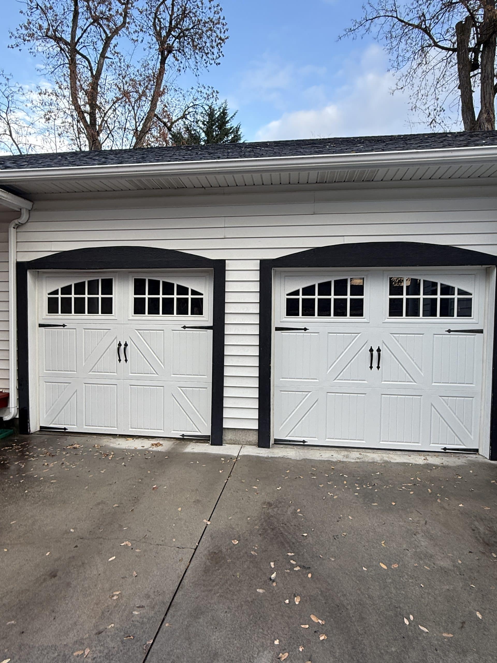 A white double garage door with decorative black hinges and handles, giving it a carriage house look.