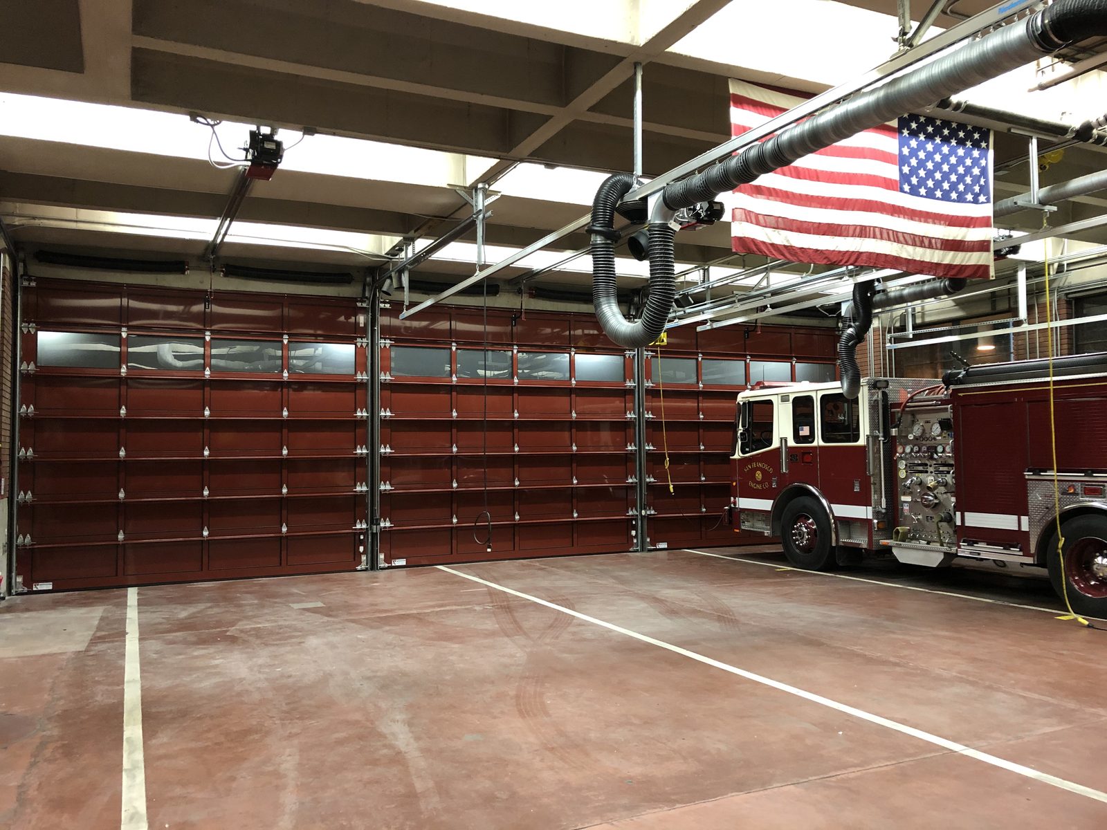 Interior view of a fire station with multiple red commercial overhead doors and a fire truck.
